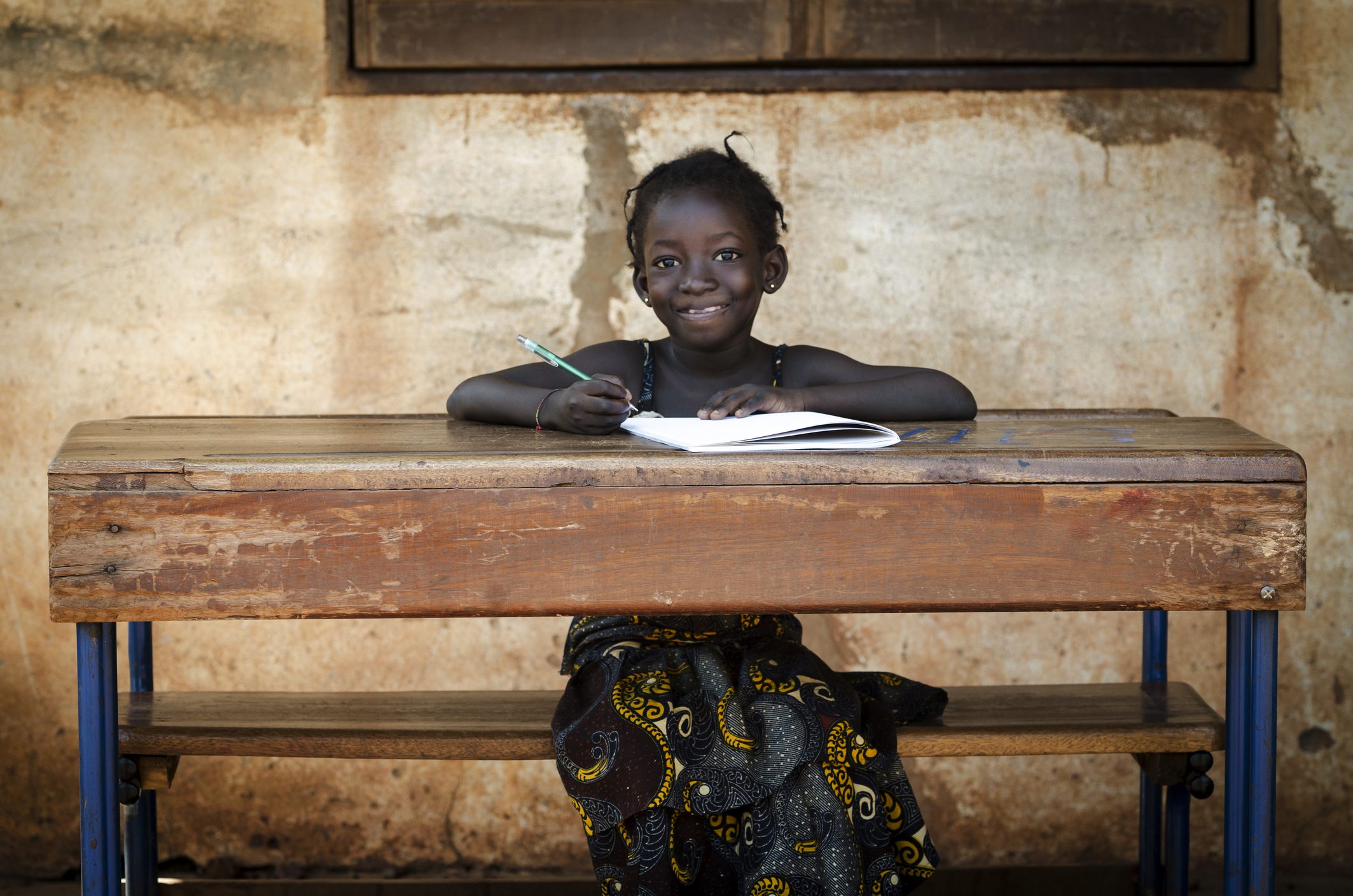 Proud African Schoolgirl Sitting In Her Desk Smiling