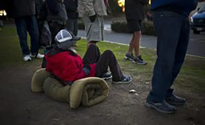 Homeless man sitting on a blanket with people walking in front